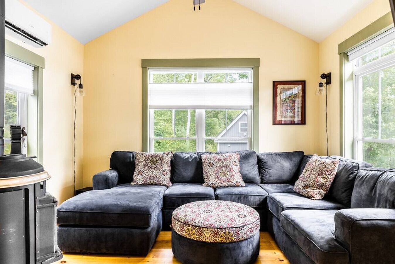 Un salon chaleureux avec un canapé d’angle et un pouf, de grandes fenêtres offrant une belle vue et une cheminée.