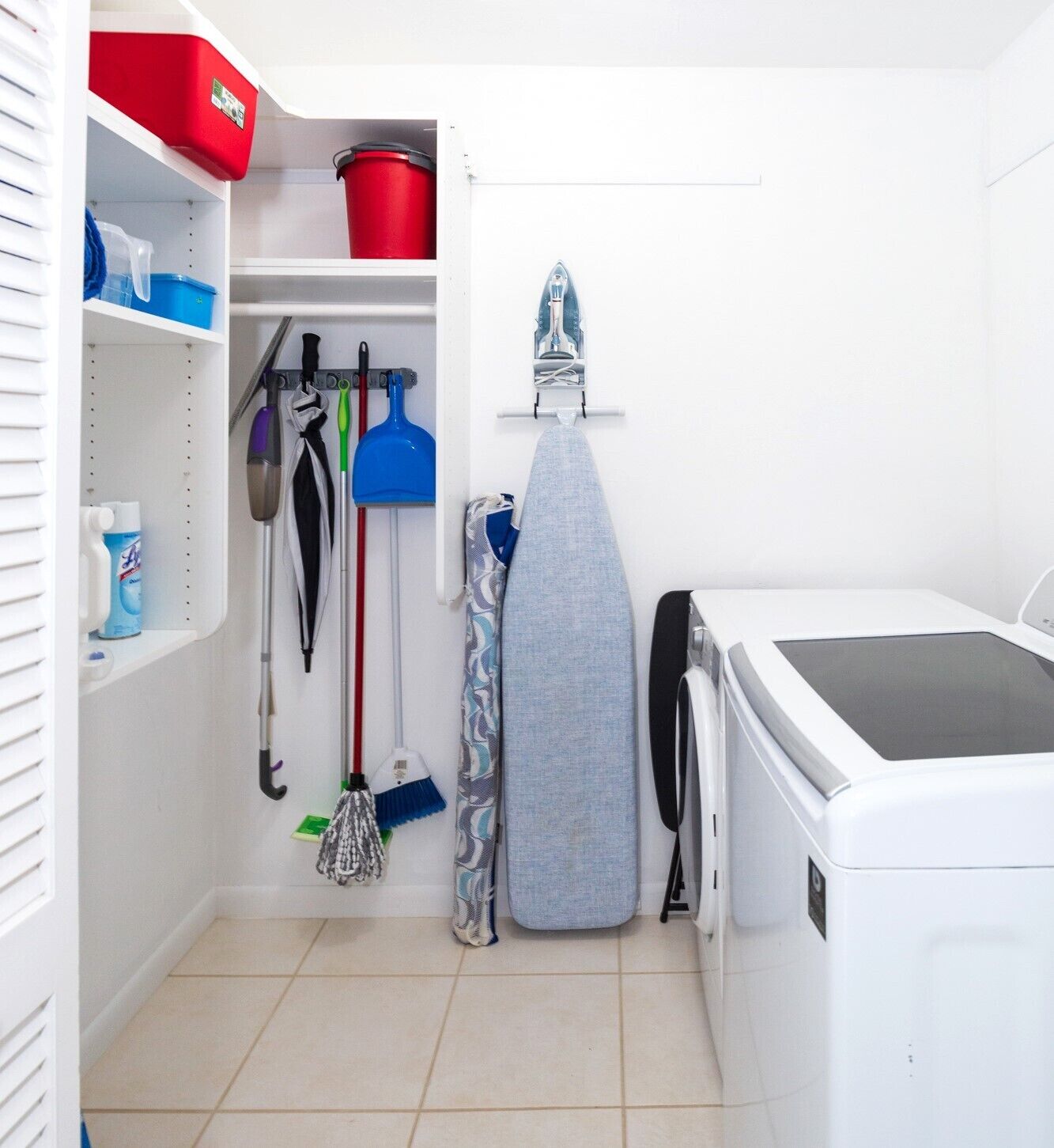 Une buanderie équipée d’un lave-linge, d’une planche à repasser et de divers outils de nettoyage.