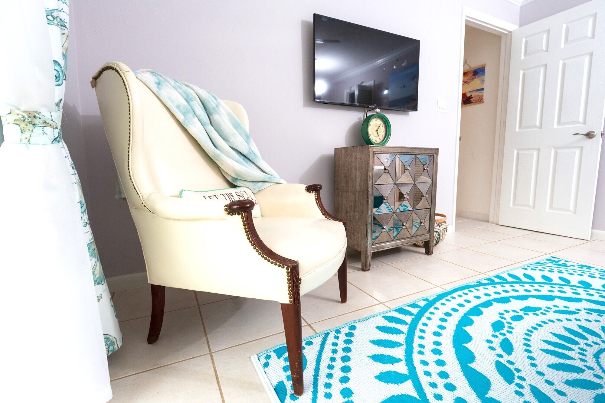 A room with a chair, a clock, a television, and a patterned rug.