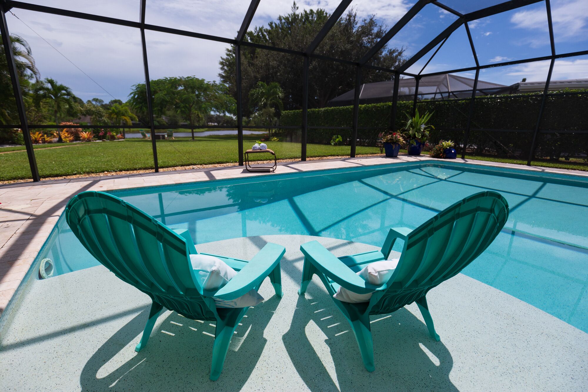A swimming pool with two green chairs and a table.