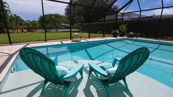 A swimming pool with two green chairs and a table.