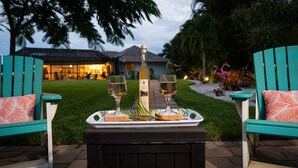 Um pátio com duas cadeiras Adirondack turquesa, um banquinho preto, uma garrafa de vinho e dois copos em um tabuleiro.