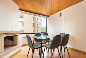 Habitació moderna amb taula i cadires de vidre, una llar de foc i vista a un edifici a través d'una finestra gran.