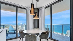 A modern dining area with a round table and four chairs, large windows with a view of the ocean and cityscape, and pendant lighting. - 2BR Oceanview HYDE – Free Parking, No Resort Fee (Hollywood)