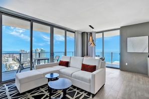 A modern living room with a white sofa, two round coffee tables, and a city view through large windows.