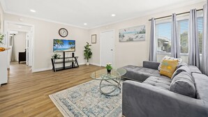 A modern living room with a grey sofa, a glass coffee table, and a wooden floor. There is a painting on the wall and a window with curtains. - Bright&Cozy Getaway 10min to Downtown LA (Alhambra)