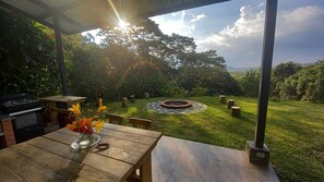 A covered patio with a stone fire pit, a grill, and a table with a vase of flowers.