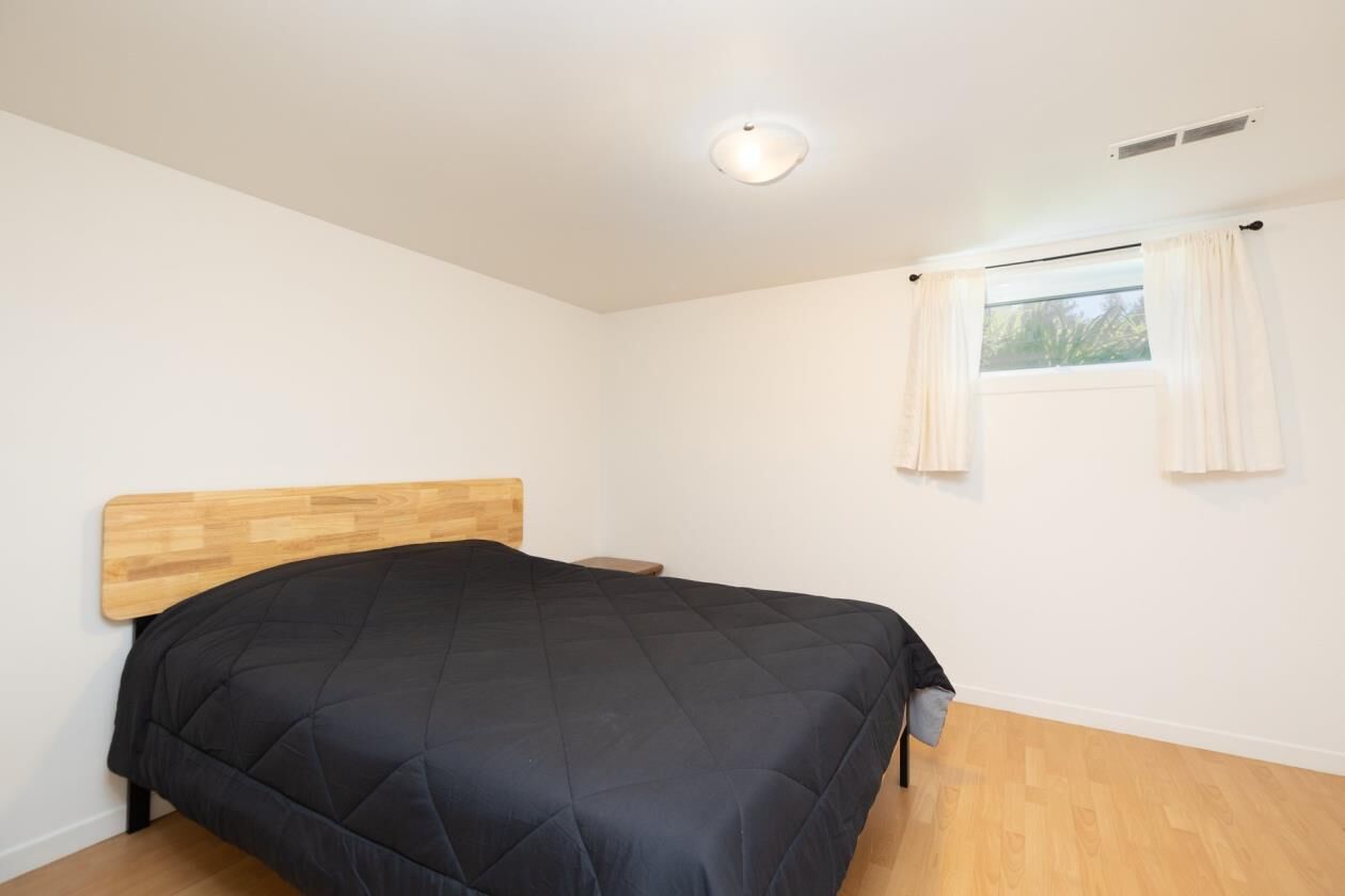 Une chambre à coucher avec une tête de lit en bois, une couvre-lit noire matelassée, une petite table de chevet et une fenêtre avec des rideaux.