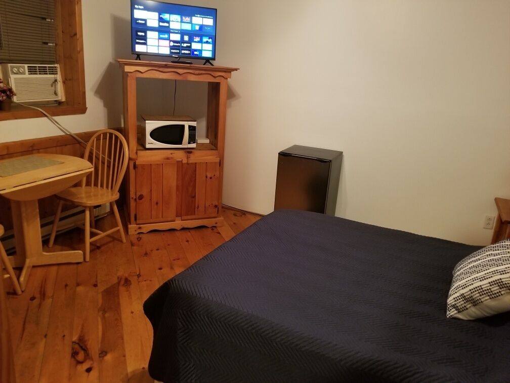 Een kamer met een bed, een houten bureau, een stoel, een televisie, een magnetron en een koelkast.