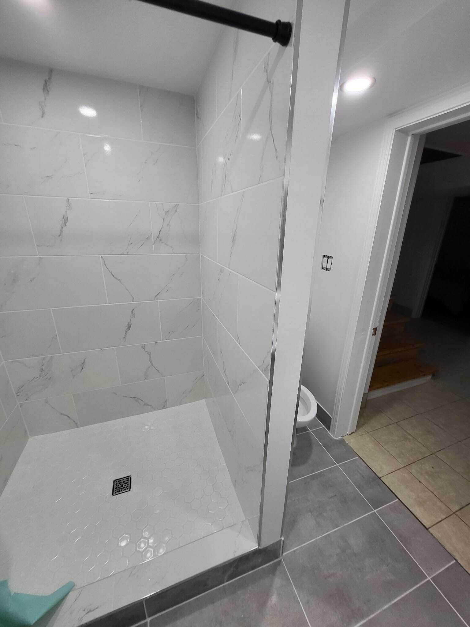 A shower area with a glass door, white marble tiles, and a visible drain.