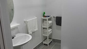 A bathroom with a white sink, a mirror, a towel rack, a shelf with toiletries, and a toilet.