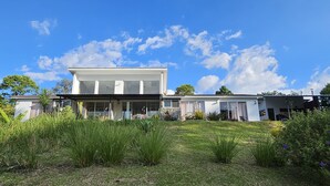 Une maison moderne à deux étages, dotée d’une grande pelouse à l’avant, d’un patio couvert et d’un petit jardin.