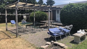 Ein überdachter Patio-Bereich mit Tisch und Stühlen, einer Schaukel und einem kleinen Blumenbeet mit Steinen.