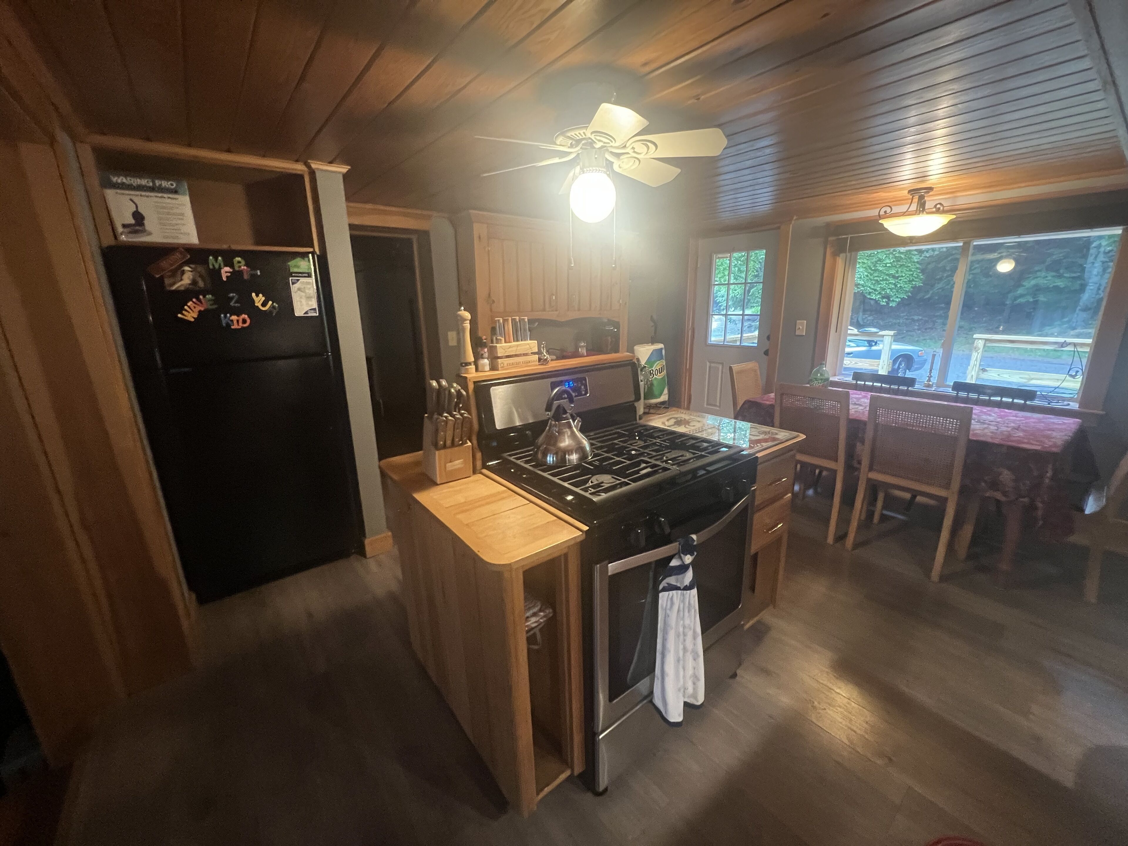 A kitchen with wooden cabinets, a black refrigerator, a stove, and a dining area with a table and chairs.