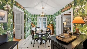 Un coin repas avec une table ronde, des chaises et un lustre. On y trouve un meuble sur lequel sont posés une lampe et une petite statue.