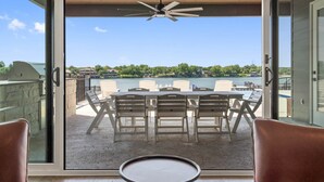 A balcony with a table and chairs, a ceiling fan, and a view of a lake and surrounding houses. - Waterhouse at Lake LBJ Residence III 6 King Beds, Pool/Spa, Boat/PWC Lift, Slide (Kingsland)
