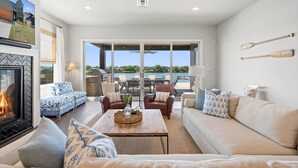 A spacious living room with a fireplace, comfortable seating, and a large window overlooking a scenic outdoor area. - Waterhouse at Lake LBJ Residence III 6 King Beds, Pool/Spa, Boat/PWC Lift, Slide (Kingsland)