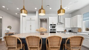 A kitchen with a central island, white cabinets, and a hanging light fixture. - Waterhouse at Lake LBJ Residence III 6 King Beds, Pool/Spa, Boat/PWC Lift, Slide (Kingsland)