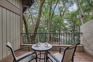 A balcony with a round table and four chairs, overlooking a forested area.