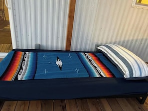 Un lit avec une couverture colorée et un oreiller à rayures, placé devant un mur en métal ondulé.
