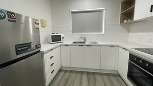 Una cocina moderna con gabinetes blancos, un refrigerador de acero inoxidable, un microondas, un fregadero y un horno.