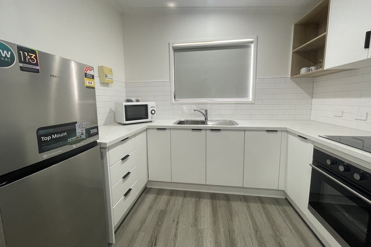 A modern kitchen with white cabinets, a stainless steel refrigerator, a microwave, a sink, and an oven.