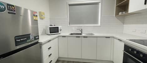 Eine moderne Küche mit weißen Schränken, einem Edelstahlkühlschrank, einer Mikrowelle, einer Spüle und einem Backofen.