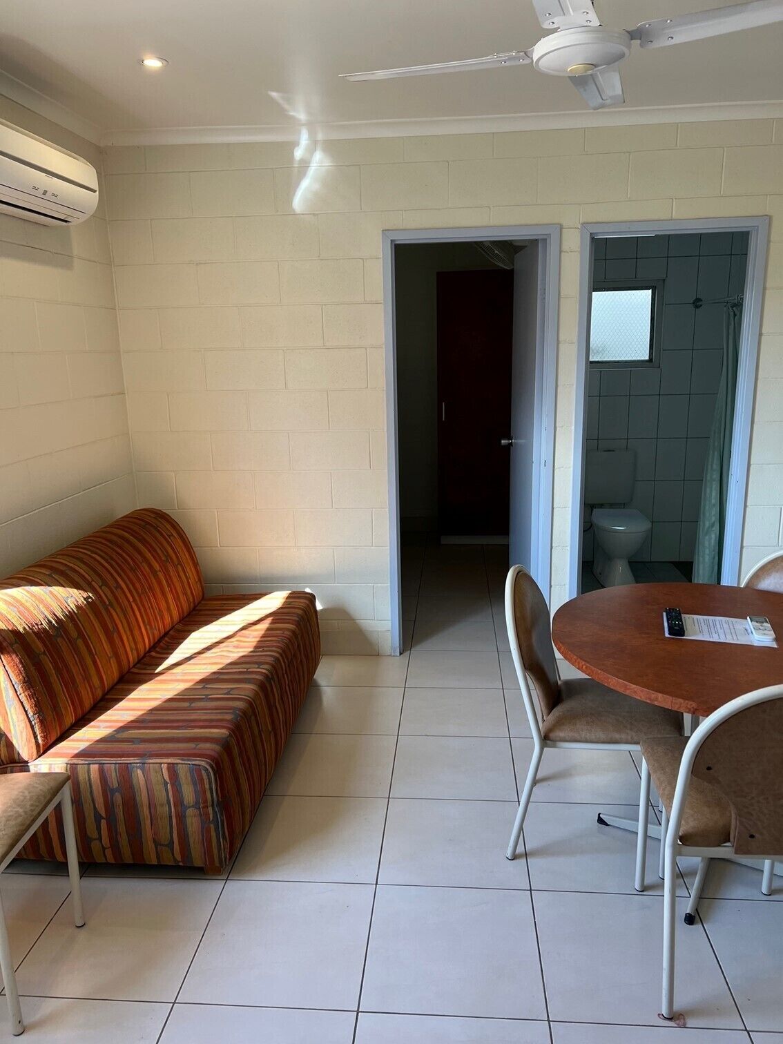 A room with a sofa, a dining table with chairs, a ceiling fan, and a window.