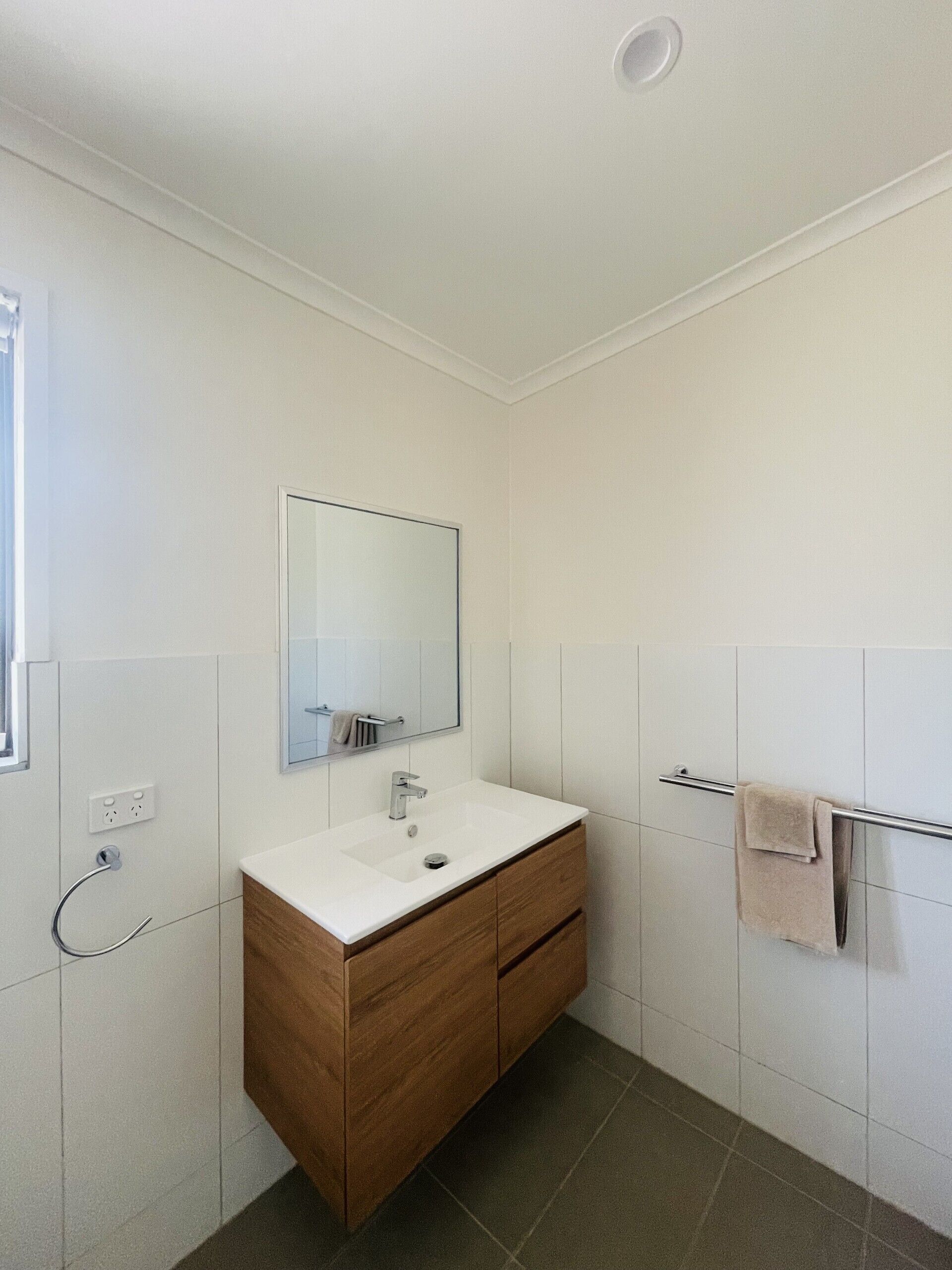A modern bathroom with a white vanity, a mirror, a towel rack, and a shower area.