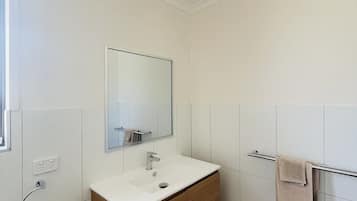 A modern bathroom with a white vanity, a mirror, a towel rack, and a shower area.
