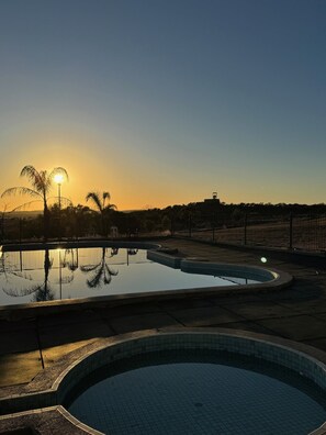 Una piscina al atardecer con reflejos nítidos, rodeada de una valla y palmeras.