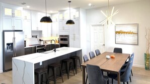 Een moderne keuken met witte kasten, een centraal eiland en een eetgedeelte met een houten tafel en stoelen.