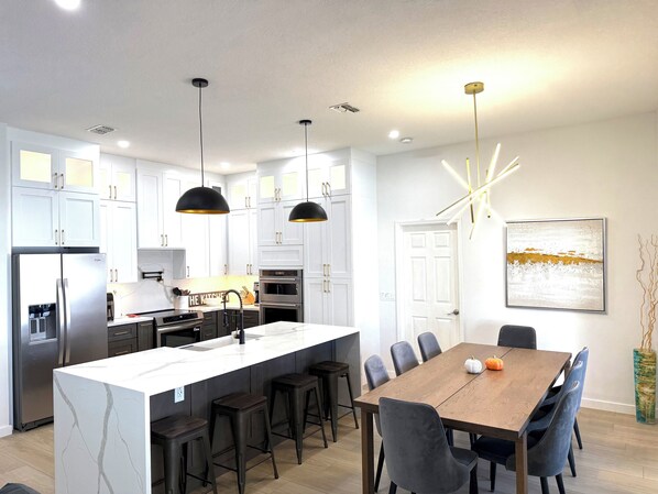 A modern kitchen with white cabinets, a central island, and a dining area with a wooden table and chairs.