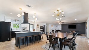 Una cocina moderna con una isla central, taburetes de bar y una zona de comedor con una mesa grande y sillas.