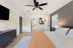 Ein modernes Schlafzimmer mit einem Bett, einem Deckenventilator, einem Fernseher und einer Kommode.