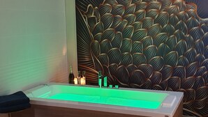 A modern bathroom with a rectangular bathtub, a decorative wall with a leaf pattern, and a green-lit water feature. - La Bulle d'Or-House-Deluxe-Whirlpool bath-Garden view (Francueil)