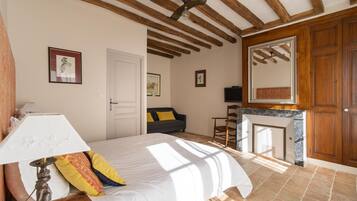 Ein Schlafzimmer mit Bett, Nachttisch, Lampe, Sofa, Sessel, Kamin und Holzbalken an der Decke.