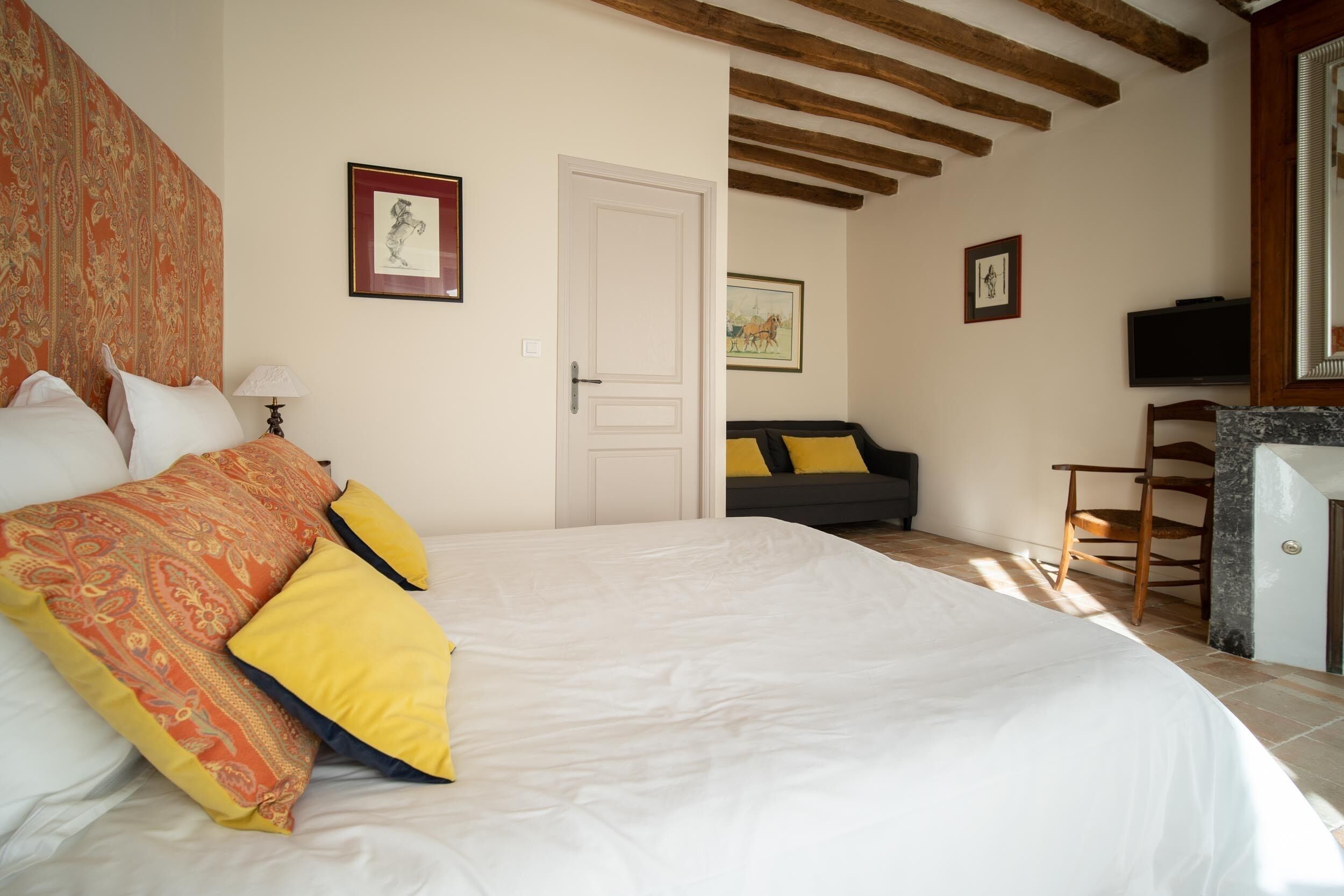 A bedroom with a large bed, a sofa, a television, and a door leading to another room.