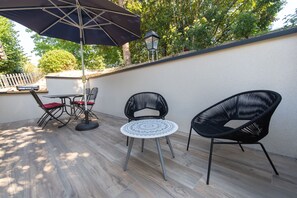 Un patio exterior con una mesa, sillas, un parasol grande y una lámpara fijada a la pared.