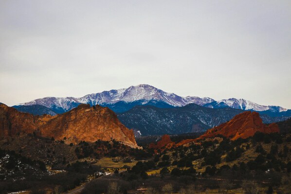 A mountainous landscape with prominent red rock formations and snow-capped peaks in the background.