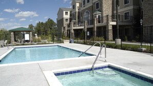 A swimming pool with a metal ladder, surrounded by a stone building with balconies and a covered seating area. - Suite Near Pikes National Forest | Outdoor Pool (Colorado Springs)