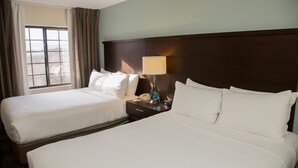 A hotel room with two beds, a nightstand with a lamp, and a window with curtains. - Suite Near Pikes National Forest | Outdoor Pool (Colorado Springs)
