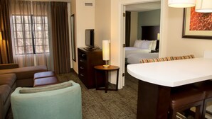 A hotel room with a sofa, a small table with a lamp, a bed, and a desk with a chair. - Suite Near Pikes National Forest | Outdoor Pool (Colorado Springs)