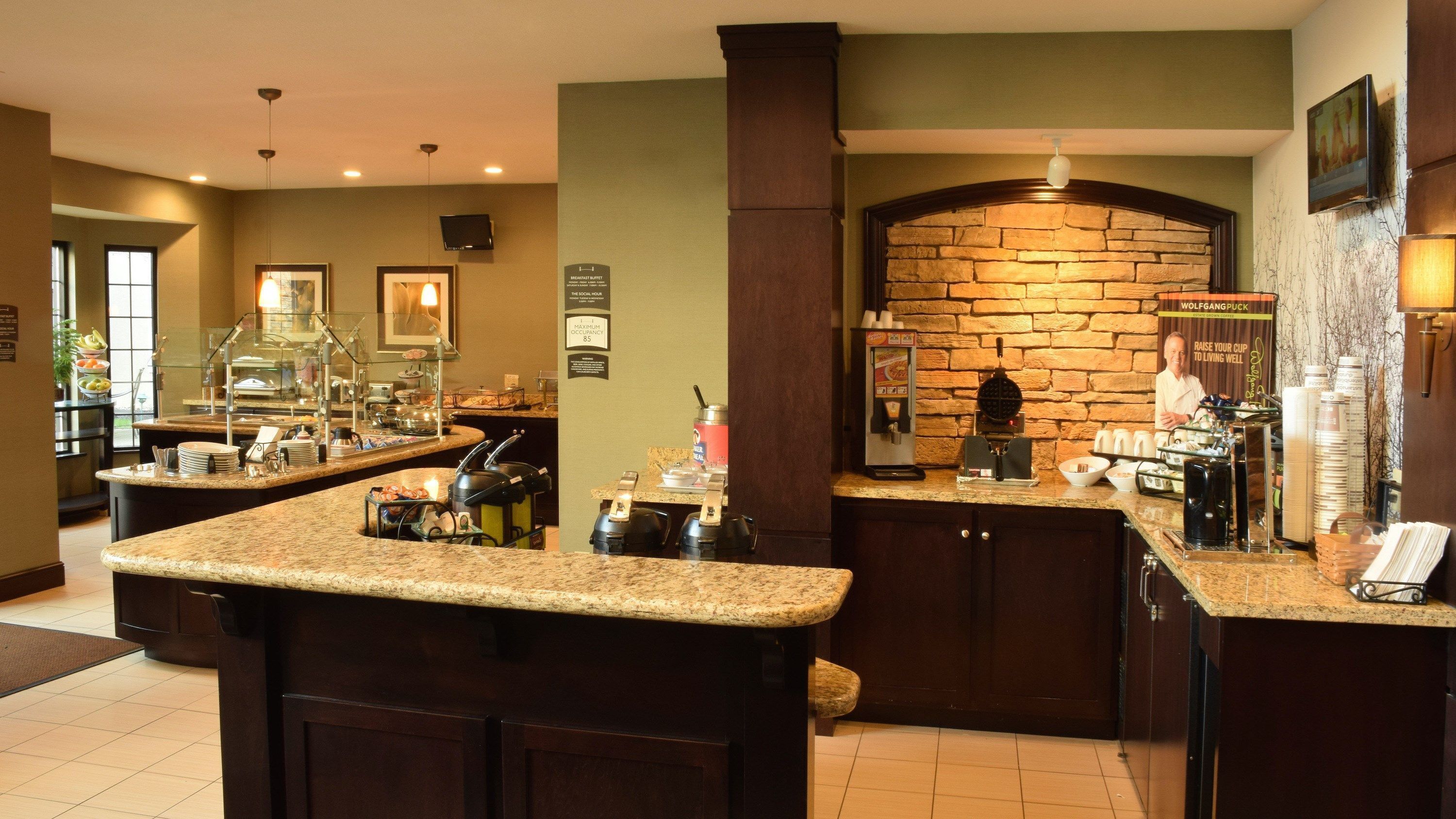 A hotel kitchen with granite countertops, a stone backsplash, and a coffee station.