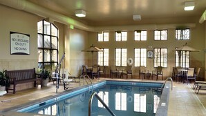Zona de piscina amb cadires i taules, un cartell de socorrista i grans finestres.
