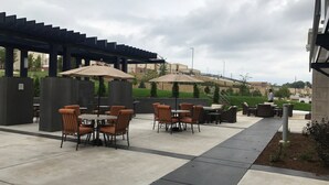 Un espace extérieur aménagé en terrasse, avec des tables et des chaises, des parasols et une vue sur un bâtiment situé au loin.