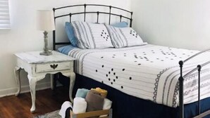 Une chambre à coucher avec un lit, une table de chevet, une lampe et une petite commode en bois.
