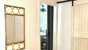 Une pièce avec un plancher en bois, un miroir doté d’un cadre décoratif, une porte coulissante et une poubelle.