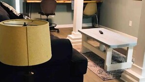 Ein Wohnzimmer mit einer Couch, einem Couchtisch, einer Lampe, einem Fernseher und einem Schreibtisch mit einem Stuhl.