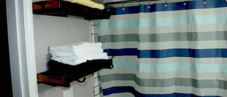 A bathroom with a striped shower curtain, a towel rack with folded towels, and a shelf with a towel.